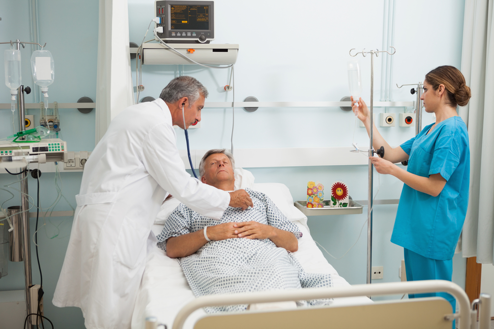 Doctor checking heart beat of patient in bed with stethoscope with nurse adjusting I-1